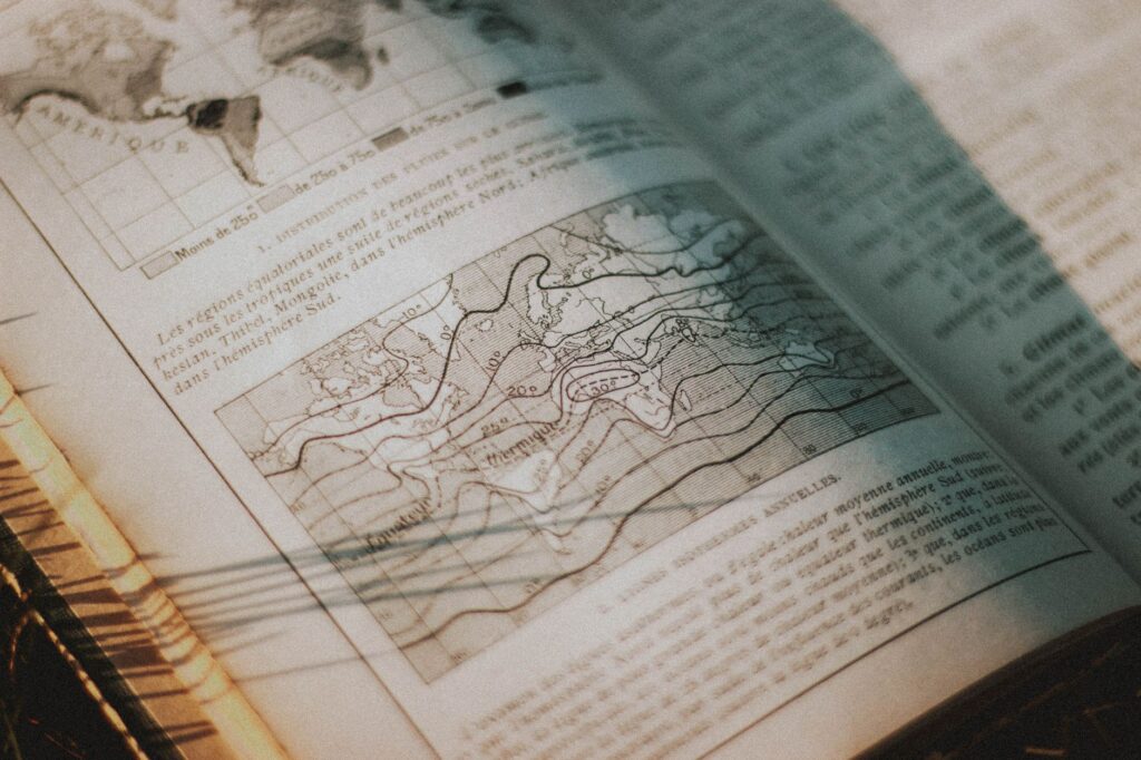 From above pages of opened book with letters and maps placed on grassy ground in rural area with bright sunlight in countryside