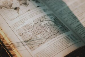 From above pages of opened book with letters and maps placed on grassy ground in rural area with bright sunlight in countryside