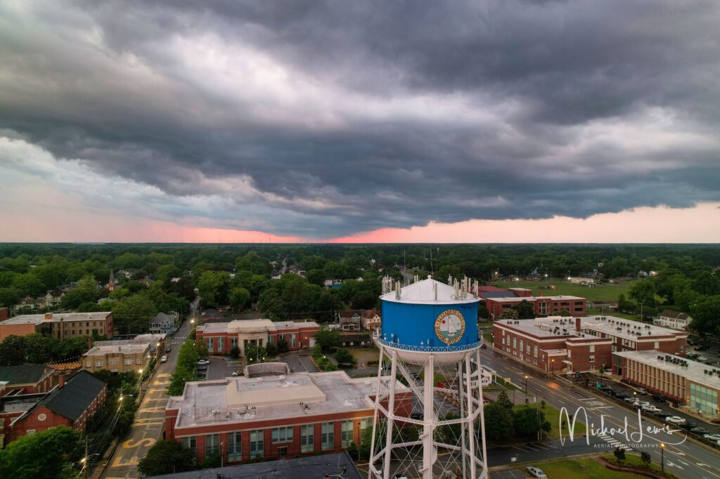 Dramatic aerial shot of a town featuring a blue water tower under moody sunset skies.