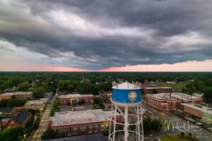 Dramatic aerial shot of a town featuring a blue water tower under moody sunset skies.