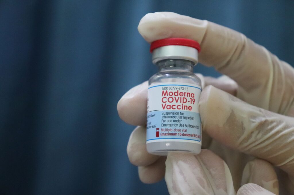 Close-up of gloved hand holding a Moderna COVID-19 vaccine vial, symbolizing immunization and protection.