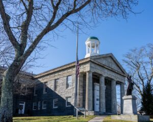 Front view of the historic Barnstable County Courthouse with a prominent statue and flag.