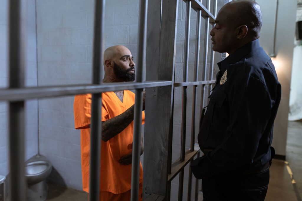 A guard converses with an inmate inside a prison cell, highlighting the justice system setting.